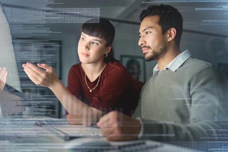 A manager helps an employee with a programming task in front of a computer
